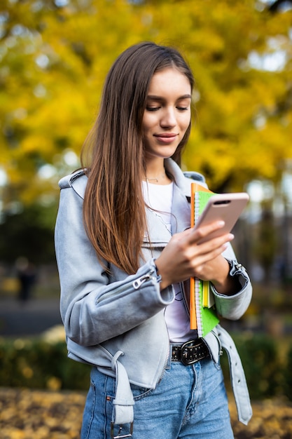 Młoda ładna kobieta studentka przeglądała telefon komórkowy idąc ulicą miasta