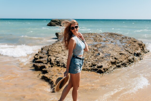 Młoda ładna kobieta w sukni i słomkowy kapelusz spaceru onocean plaży