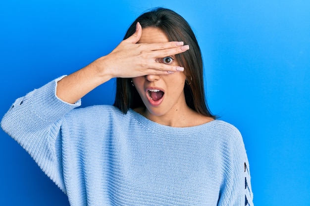 Bezpłatne zdjęcie młoda latynoska dziewczyna ubrana w zwykłe ubrania zerkająca w szoku zakrywająca twarz i oczy ręką patrzącą przez palce z zawstydzonym wyrazem twarzy