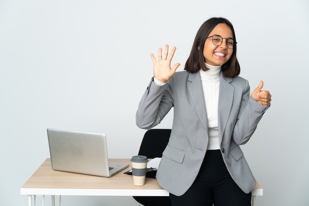 Młoda latynoska kobieta biznesu pracująca w biurze na białym tle licząc sześć palcami