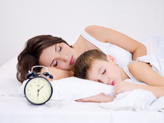 Młoda matka i syn śpi na łóżku. Ð zegar larmowy na pierwszym planie