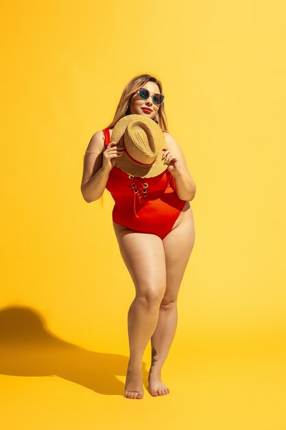 Młoda modelka rasy kaukaskiej plus size przygotowuje się do nadmorskiego kurortu na żółto