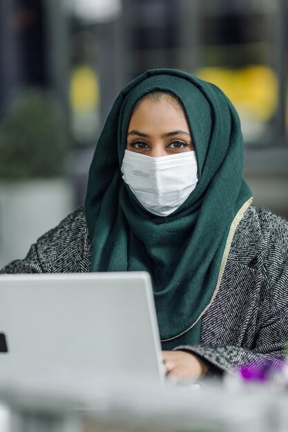 Młoda muzułmanka siedzi w ulicznej kawiarni i patrzy na laptopa