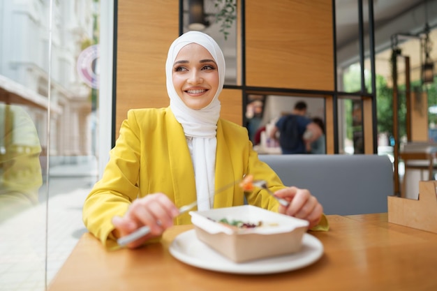 Młoda muzułmanka w hidżabie jedząca lunch w kawiarni