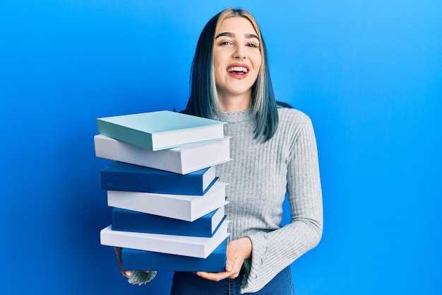Bezpłatne zdjęcie młoda nowoczesna dziewczyna trzyma stos książek uśmiechając się i śmiejąc się głośno, ponieważ zabawny szalony żart