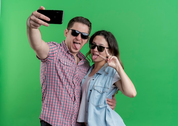 Młoda Para Mężczyzna I Kobieta W Ubranie Stojących Razem Robi Selfie Szczęśliwy W Miłości Zabawy Na Zielonej ścianie