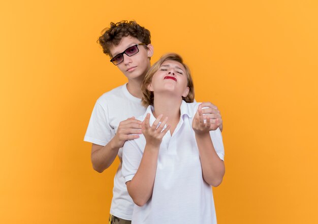 Młoda para mężczyzna próbuje przytulić swoją niezadowoloną i zdenerwowaną dziewczynę stojącą nad pomarańczową ścianą