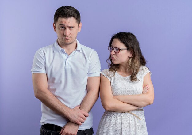 Młoda para niezadowolona kobieta patrząc na swojego zdezorientowanego chłopaka stojącego nad niebieską ścianą