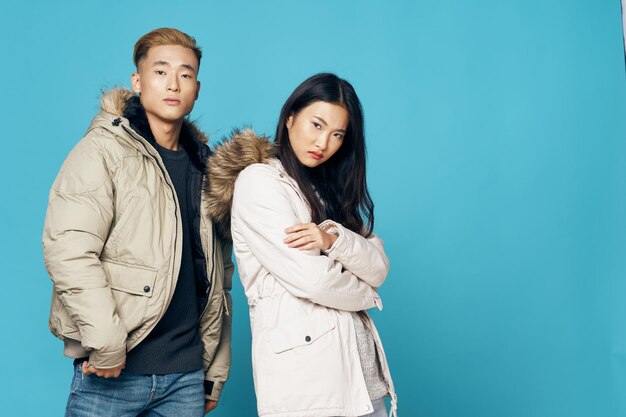 Młoda para o azjatyckim wyglądzie w zimowych kurtkach pozowanie na niebieskim tle