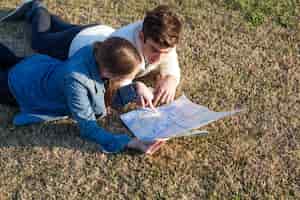 Bezpłatne zdjęcie młoda para sprawdzanie mapy leżącej na trawie