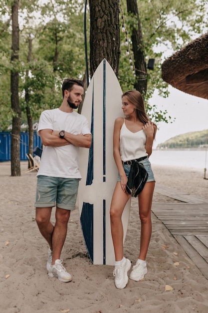 Młoda para stylowe na sobie koszulki i szorty spaceru na zewnątrz w parku w pobliżu deski surfingowej