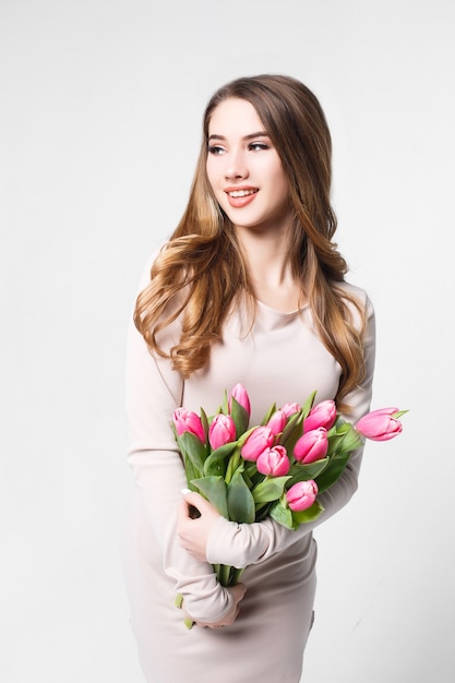 Młoda piękna blondynka z bukietem różowych tulipanów na białej ścianie