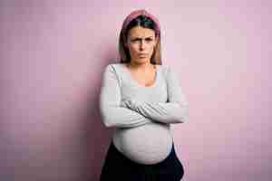Bezpłatne zdjęcie młoda piękna brunetka kobieta w ciąży spodziewa się dziecka na odizolowanym różowym tle sceptyk i nerwowy wyraz dezaprobaty na twarzy ze skrzyżowanymi ramionami osoba negatywna