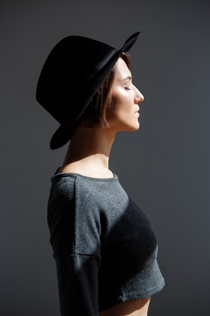 Młoda piękna brunetki dziewczyna w czarnego kapeluszu pozyci w profilu.