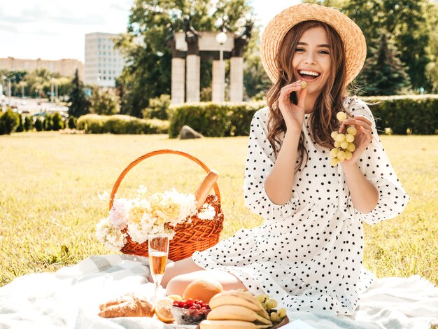 Młoda piękna dziewczyna hipster w modnej letniej sukience i kapeluszu. Beztroska kobieta robi piknik na zewnątrz.