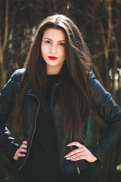 Młoda piękna dziewczyna pozuje w czarnej skórzanej kurtce w parku