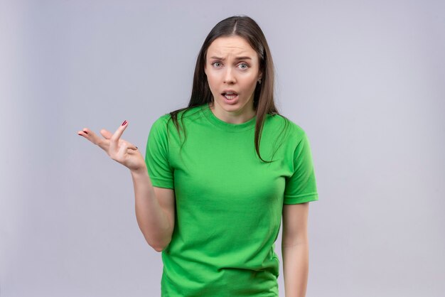 Młoda piękna dziewczyna ubrana w zielony t-shirt stojący z podniesioną ręką, zadając pytanie lub argumentując stojąc na białym tle