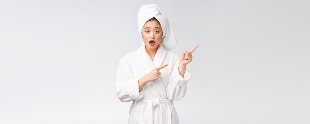 Młoda piękna kobieta nosi ręcznik pod prysznic po kąpieli na odosobnionym białym tle, wskazując palcem