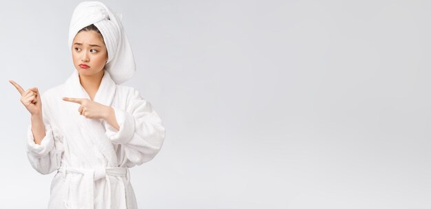Młoda piękna kobieta nosi ręcznik pod prysznic po kąpieli na odosobnionym białym tle, wskazując palcem