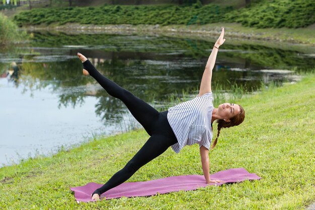 Młoda piękna kobieta robi ćwiczenia jogi w zielonym parku. Pojęcie zdrowego stylu życia i fitness.
