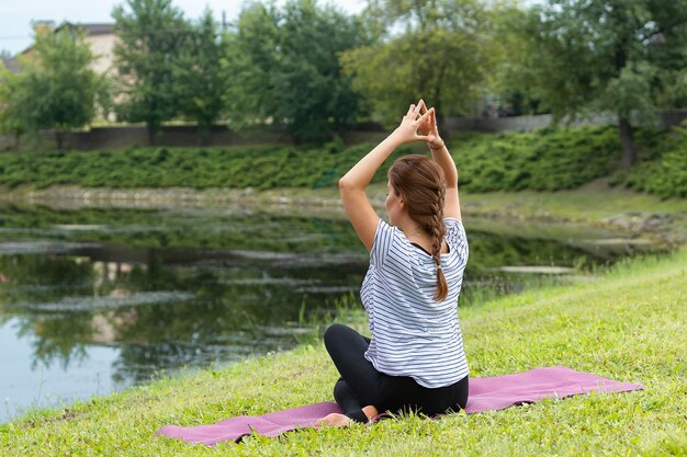 Młoda piękna kobieta robi ćwiczenia jogi w zielonym parku. Pojęcie zdrowego stylu życia i fitness.