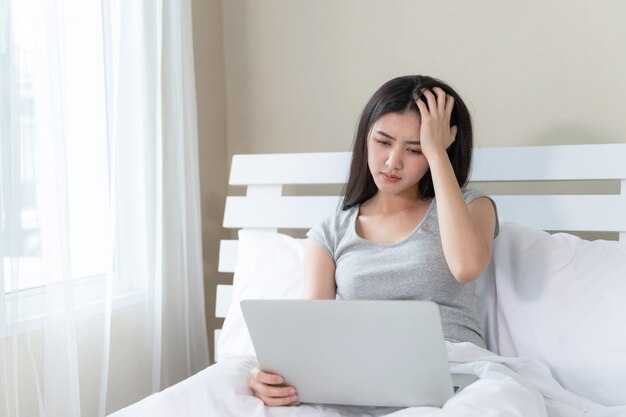 Młoda piękna kobieta siedzi na łóżku, używa laptopa czuć się poważnie i ból głowy