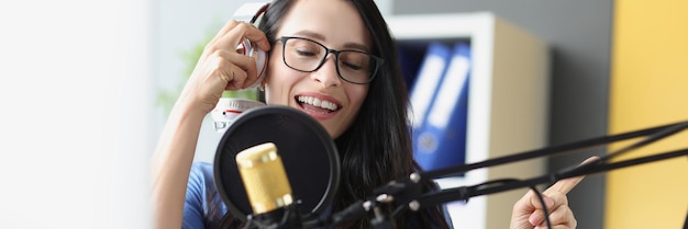Młoda piękna kobieta śpiewa do mikrofonu ze słuchawkami nagrywając piosenkę w studio