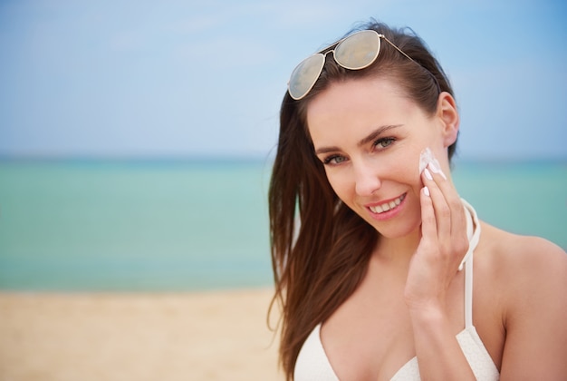 Młoda piękna kobieta stosując krem do opalania na plaży