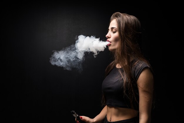 Młoda piękna kobieta vaping e - papierosa na czarnej ścianie