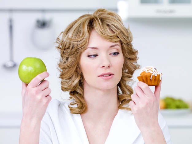 Bezpłatne zdjęcie młoda piękna kobieta wybiera między słodkim ciastem a zielonym jabłkiem