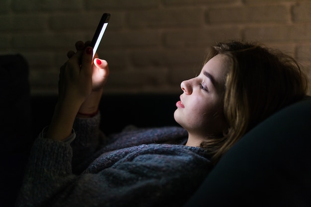 Młoda piękna kobieta za pomocą inteligentnego telefonu w nocy w łóżku - technologia, sieć społecznościowa, koncepcja bezsenności
