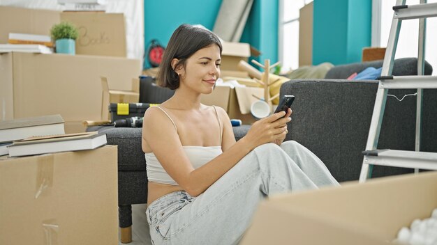 Młoda piękna Latynoska używająca smartfona siedzącego na podłodze w nowym domu