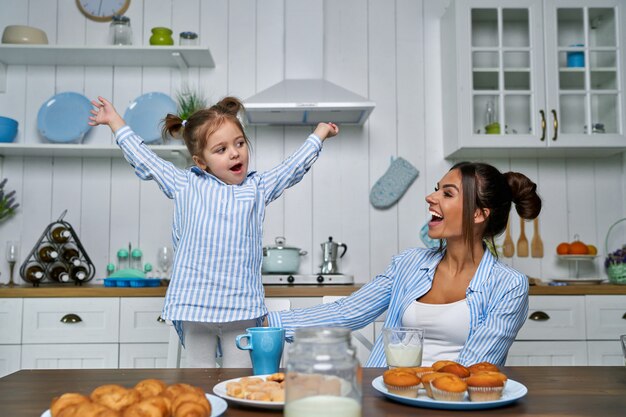 Młoda piękna matka i jej córeczka bawiące się w kuchni podczas śniadania w domu.