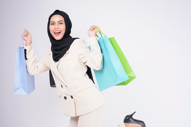 Młoda piękna muzułmańska kobieta w garniturze trzymająca kolorowe torby na zakupy na białym tle studio