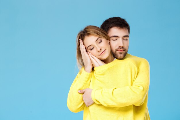 Młoda piękna para w jeden żółty sweter obejmując uśmiecha się nad niebieską ścianą