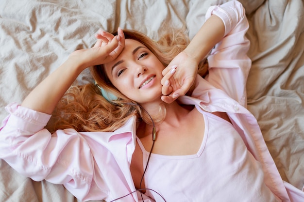 Młoda piękna ruda dziewczyna w słuchawkach rozciągająca się w łóżku po przebudzeniu w pełni wypoczęta.