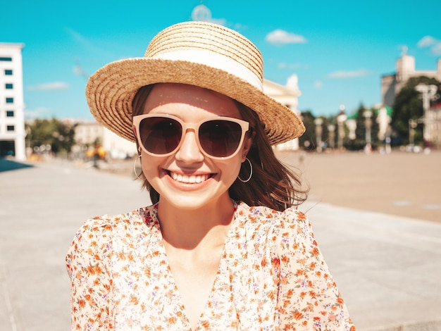 Młoda piękna uśmiechnięta kobieta hipster w modnych letnich ubraniach Seksowna beztroska kobieta pozuje na tle ulicy w plażowym kapeluszu o zachodzie słońca Pozytywny model na zewnątrz Wesoły i szczęśliwy w okularach przeciwsłonecznych