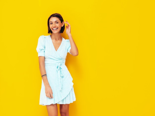 Młoda piękna uśmiechnięta kobieta w modnej letniej niebieskiej sukience Seksowna beztroska kobieta pozuje w pobliżu żółtej ściany w studio Pozytywny model zabawy Wesoły i szczęśliwy na białym tle