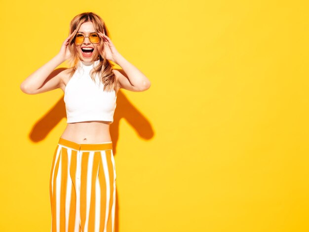 Młoda piękna uśmiechnięta kobieta w modnych letnich ubraniach Seksowna beztroska kobieta pozuje w pobliżu niebieskiego żółtego w studio Pozytywny model zabawy Wesoły i szczęśliwy w okularach przeciwsłonecznych Krzyki i krzyki