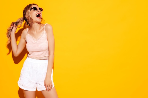 Młoda piękna uśmiechnięta kobieta w modnych letnich ubraniach Seksowna beztroska kobieta pozuje w pobliżu niebieskiego żółtego w studio Pozytywny model zabawy Wesoły i szczęśliwy w okularach przeciwsłonecznych Krzyki i krzyki