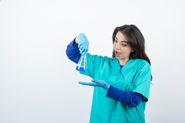 Młoda pielęgniarka w medycznych rękawiczkach trzyma butelkę chemiczną.