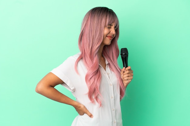 Młoda piosenkarka rasy mieszanej z różowymi włosami na zielonym tle, cierpiąca na ból pleców za wysiłek