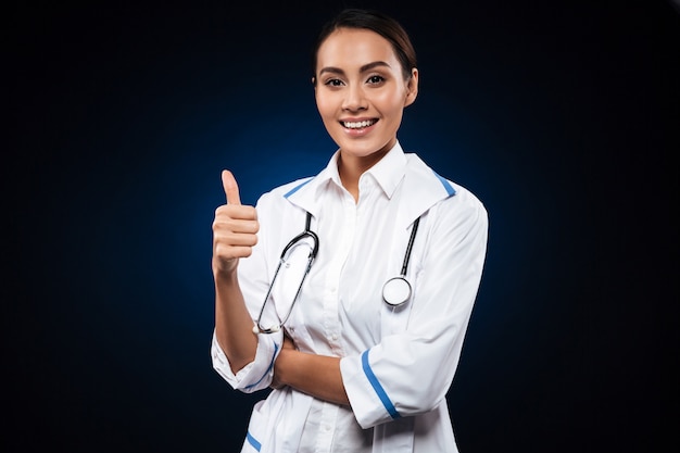 Młoda pozytywna kobiety lekarka z stetoskopem pokazuje kciuk up