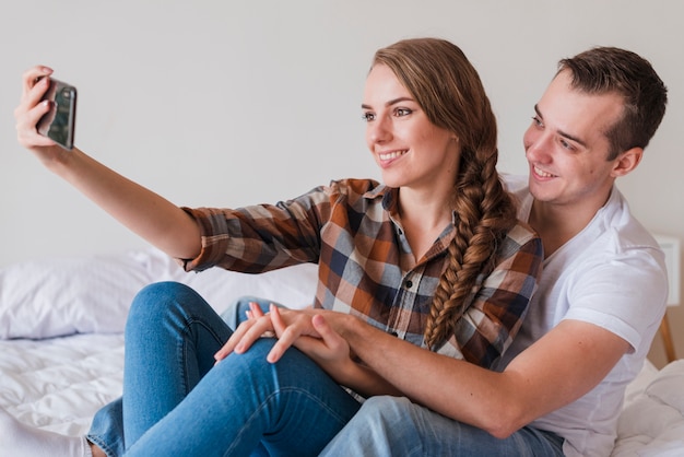 Bezpłatne zdjęcie młoda pozytywna para bierze selfie w sypialni w domu