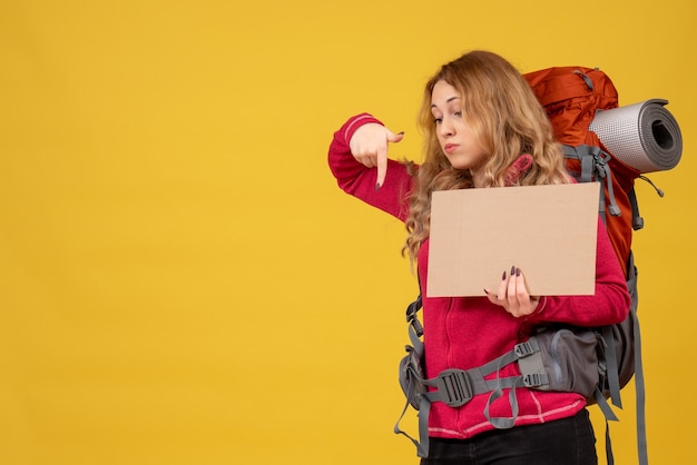 Bezpłatne zdjęcie młoda przemyślana podróżująca dziewczyna zbierająca swój bagaż, pokazująca wolne miejsce do pisania i wskazywania w dół
