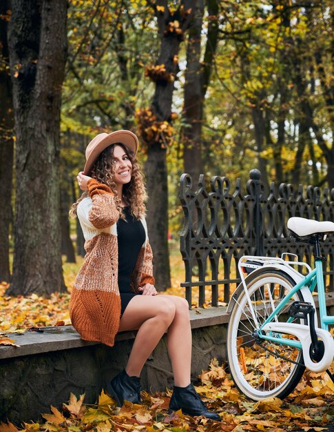 Młoda rowerzystka odpoczywa na krawężniku w pobliżu roweru na jesień