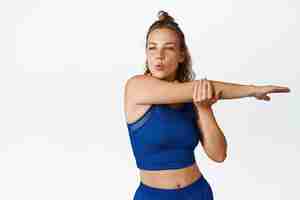 Bezpłatne zdjęcie młoda sportowa kobieta kontroluje oddychanie, wyciągając rękę. dziewczynka fitness rozgrzewa się, robi trening dla zdrowego ciała, stojąc w odzieży sportowej na białym tle