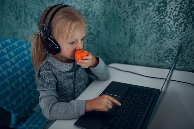 Młoda studentka mała dziewczynka z marchewką w ręku i laptopem ucząca się i przygotowująca się do powrotu do szkoły