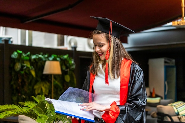 Bezpłatne zdjęcie młoda studentka ubrana w pelerynę ukończenia szkoły i patrząca na swój zeszyt