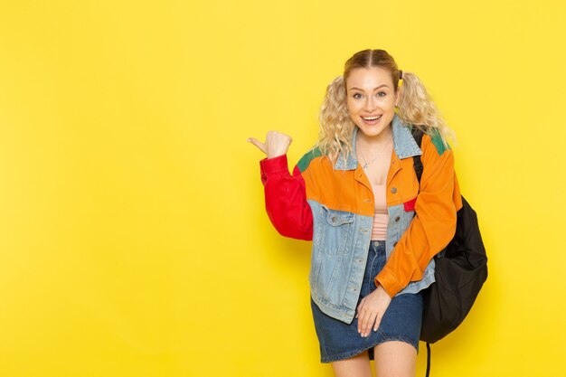młoda studentka w nowoczesne ubrania po prostu pozuje z uśmiechem, wskazując na żółty